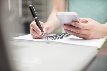 Woman writing notes in diary, holding smartphone - ZEF15380