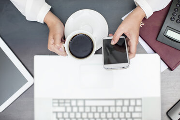 Frau mit einer Tasse Kaffee, die ein Smartphone und einen Laptop benutzt - ZEF15384