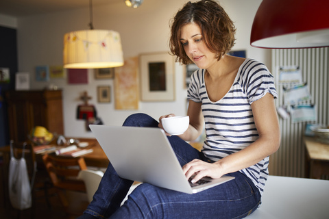 Portrait of mature woman sitting on kitchen table using laptop stock photo