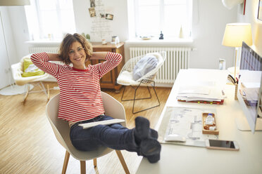 Porträt einer lächelnden reifen Frau, die sich auf einem Sessel im Heimbüro entspannt - PNEF00625