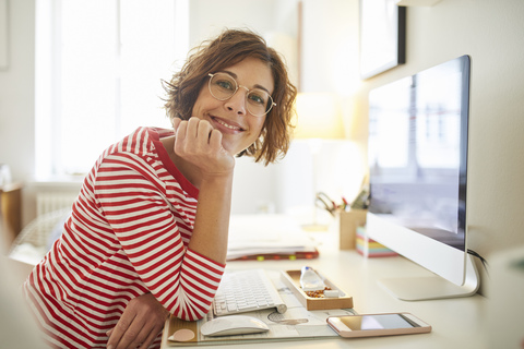 Portrait of content mature woman sitting at desk at home stock photo