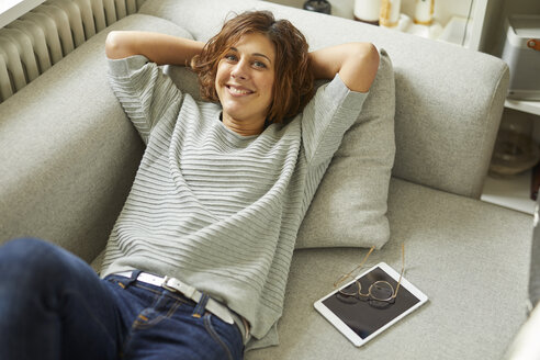 Porträt einer lächelnden reifen Frau, die sich auf der Couch entspannt - PNEF00632