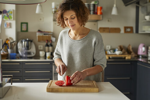 Reife Frau schneidet Tomate in der Küche - PNEF00633