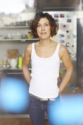 Portrait of mature woman wearing white tank top standing in the kitchen - PNEF00636