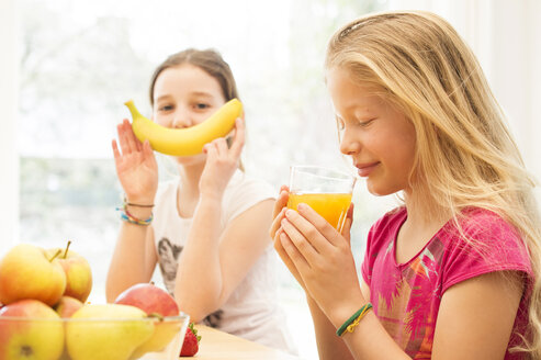 Porträt eines Mädchens, das ein Glas Orangensaft trinkt, während ihre Freundin sich mit einer Banane vergnügt - NEKF00036