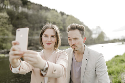 Porträt eines jungen Paares, das ein Selfie mit seinem Smartphone im Freien macht - KMKF00245