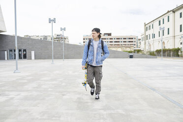 Junger Mann zu Fuß in der Stadt, mit Skateboard - FMOF00364