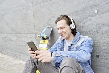 Junger Mann mit Skateboard auf dem Boden sitzend, mit digitalem Tablet - FMOF00366