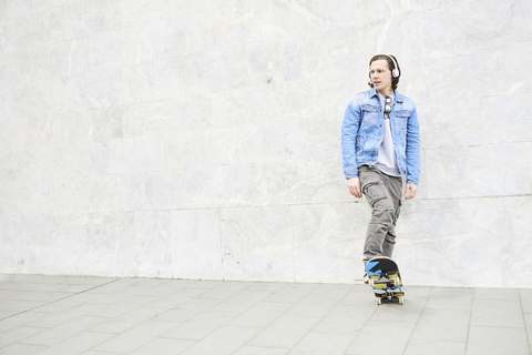 Junger Mann, der auf ein Skateboard steigt und wegschaut, lizenzfreies Stockfoto