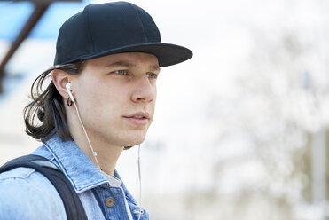 Portrait of a young man wearing baseball cap and ear buds - FMOF00378