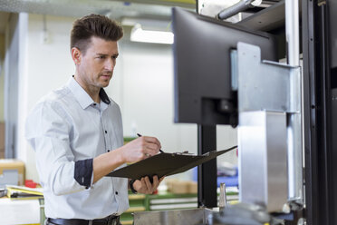 Man with clipboard in factory looking at screen - DIGF03985