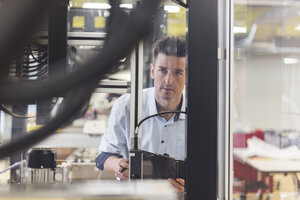 Mann mit Klemmbrett in einer Fabrik, der eine Maschine untersucht - DIGF03987