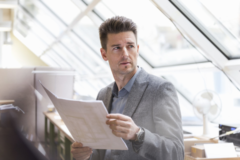 Geschäftsmann in Fabrik mit Plan, der sich umschaut, lizenzfreies Stockfoto