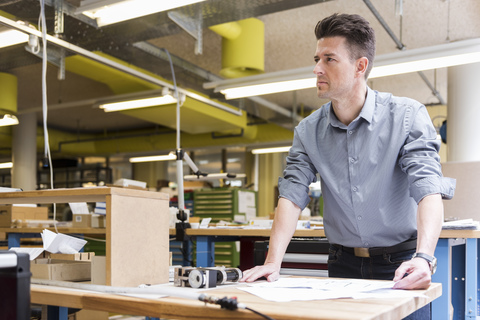 Mann in Fabrik mit Plan schaut sich um, lizenzfreies Stockfoto