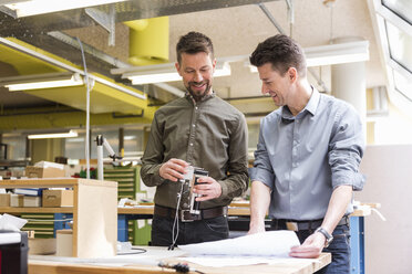 Two smiling men with plan looking at product in factory - DIGF04000