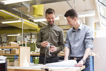Zwei lächelnde Männer mit Plan betrachten ein Produkt in einer Fabrik - DIGF04000
