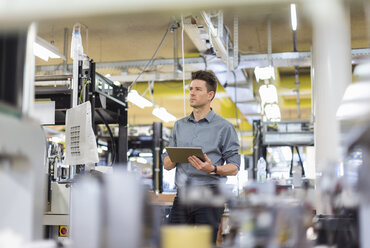 Man standing in factory with tablet looking sideways - DIGF04010