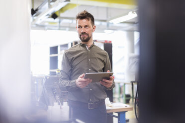 Lächelnder Mann, der in einer Fabrik mit einem Tablet steht und zur Seite schaut - DIGF04012