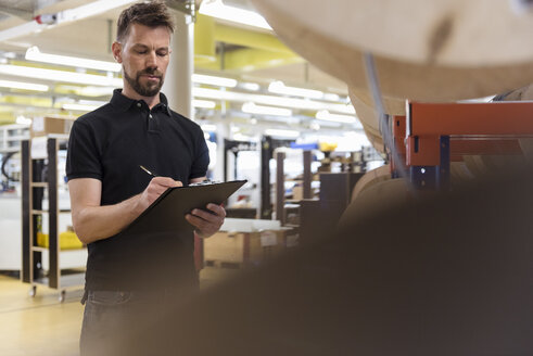 Mann mit Klemmbrett in Fabrik, der Notizen macht - DIGF04017