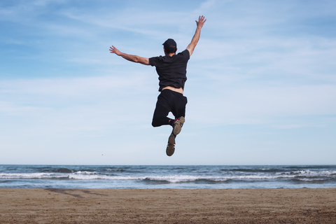 Back view of man jumping in the air on the beach stock photo