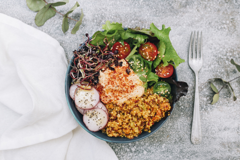 Vegane Buddha-Bowl mit Hummus, Quinoa mit Curry, Salat, Sprossen, grünen und roten Kirschtomaten, Radieschenscheiben und Sesam und Mohn, lizenzfreies Stockfoto