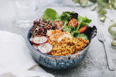 Vegane Buddha-Bowl mit Hummus, Quinoa mit Curry, Salat, Sprossen, grünen und roten Kirschtomaten, Radieschenscheiben und Sesam und Mohn, lizenzfreies Stockfoto