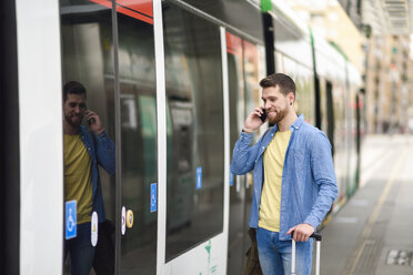 Junger Mann mit Smartphone vor einer Straßenbahn - JSMF00160