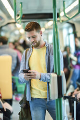 Junger Mann in einem U-Bahn-Zug, der auf sein Smartphone schaut - JSMF00162