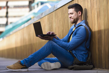 Junger Mann sitzt auf einem Steg und benutzt einen Laptop - JSMF00166