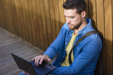Junger Mann sitzt auf einem Steg und benutzt einen Mini-Laptop - JSMF00167