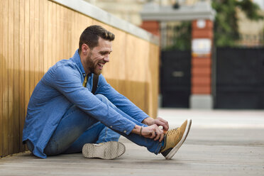 Young man laughing, sitting on footbridge - JSMF00168