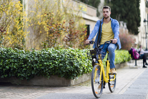 Junger Mann mit Leihfahrrad in der Stadt, lizenzfreies Stockfoto