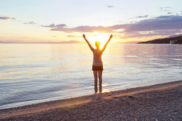 Greece, Pelion, Pagasetic Gulf, woman on the beach with raised arms at sunset, Kalamos in the background - MAMF00081