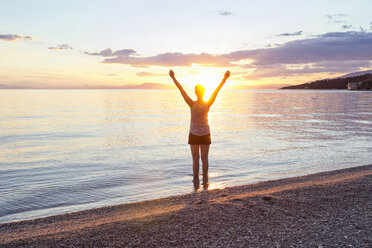 Griechenland, Pelion, Pagasetischer Golf, Frau am Strand mit erhobenen Armen bei Sonnenuntergang, Kalamos im Hintergrund - MAMF00081