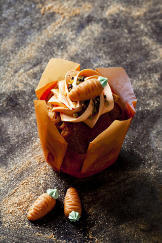 Karotten-Cupcake garniert mit Sahnehaube, Zuckergranulat und Marzipankarotte, lizenzfreies Stockfoto