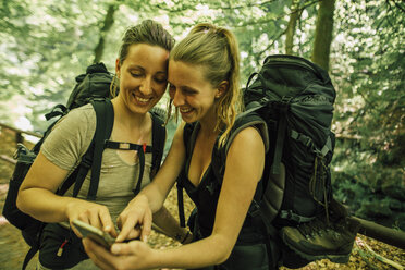 Zwei glückliche junge Frauen auf einem Wanderausflug mit Mobiltelefon - GUSF00743