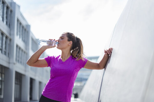 Junge Frau, die eine Pause vom Sport macht und aus einer Flasche trinkt - DIGF04052