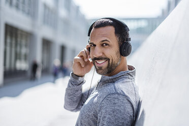 Portrait of smiling man having a break from exercising wearing headphones - DIGF04055