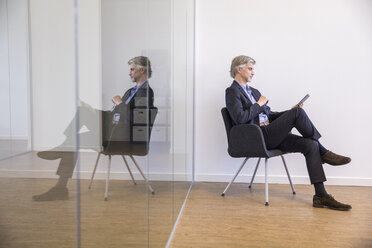 Businessman sitting on chair, using digital tablet - FMKF05020