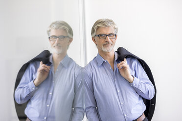 Confident businessman leaning against glass wall - FMKF05039