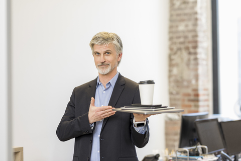 Selbstbewusster Geschäftsmann präsentiert mobile Geräte mit einer Tasse Kaffee darauf, lizenzfreies Stockfoto