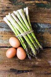 Grüner Spargel und braune Eier auf Holz - GIOF03923