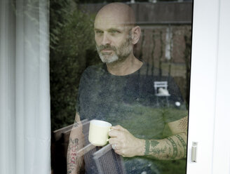 Tätowierter Mann trinkt Kaffee und schaut aus dem Fenster - FLLF00020