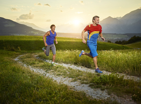 Zwei Sportler laufen bei Sonnenuntergang auf einem Feldweg, lizenzfreies Stockfoto