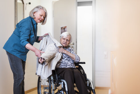 Woman taking care of old woman in wheelchair putting her jacket on - DIGF04069