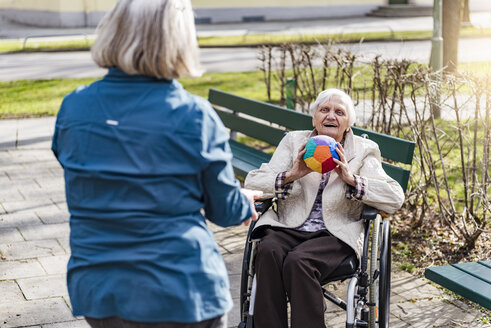 Frau kümmert sich um eine alte Frau im Rollstuhl, die im Park mit einem Ball spielt - DIGF04070