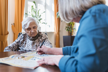 Frau kümmert sich um alte Frau bei Kreuzworträtsel - DIGF04071