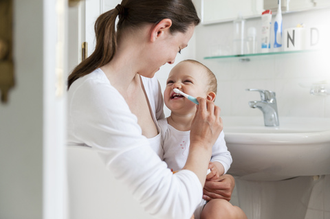 Mother brushing baby's teeth in bathroom stock photo