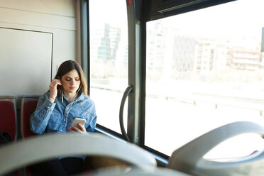 Junge Frau sitzt im Bus und hört Musik mit Handy und Kopfhörern - VABF01558