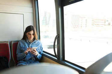 Young woman sitting in bus listening music with cell phone and earphones - VABF01559